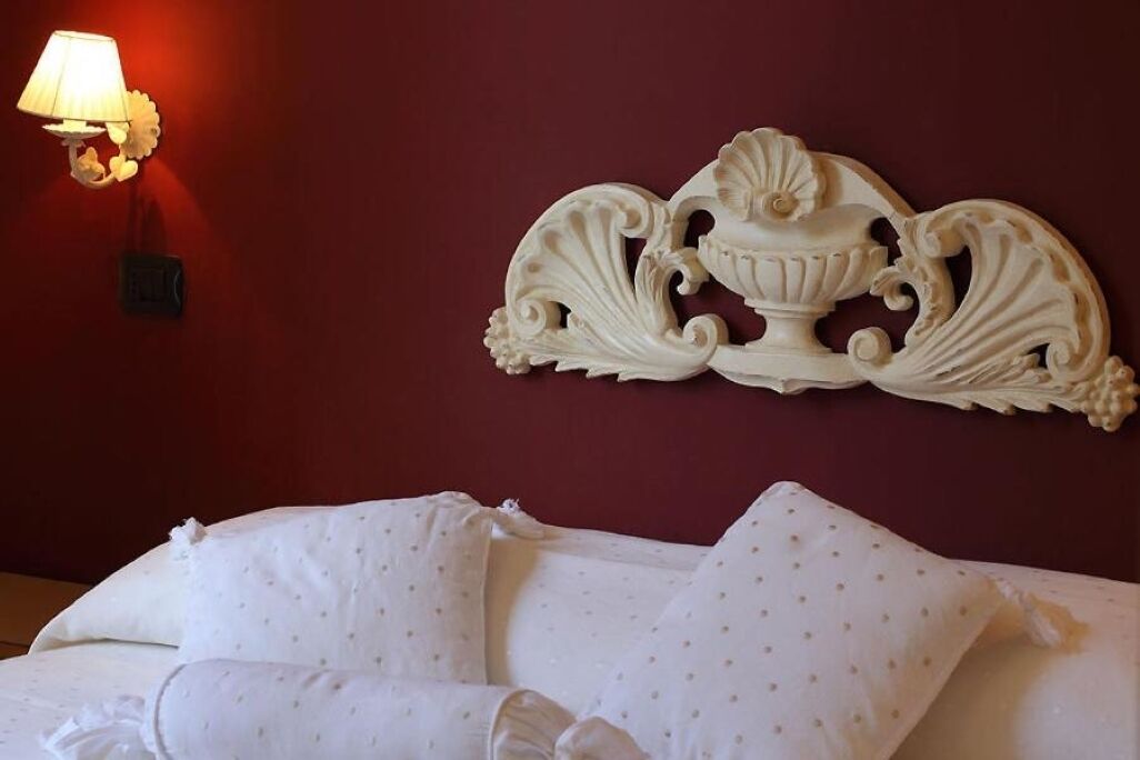 Camera d'albergo con parete rossa, un elemento decorativo a parete e un letto con cuscini e copripiumino bianchi.
