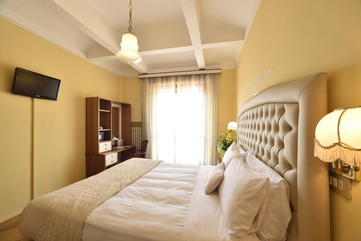 Una habitación de hotel con una cama grande, televisión, armario y ventana con cortinas.