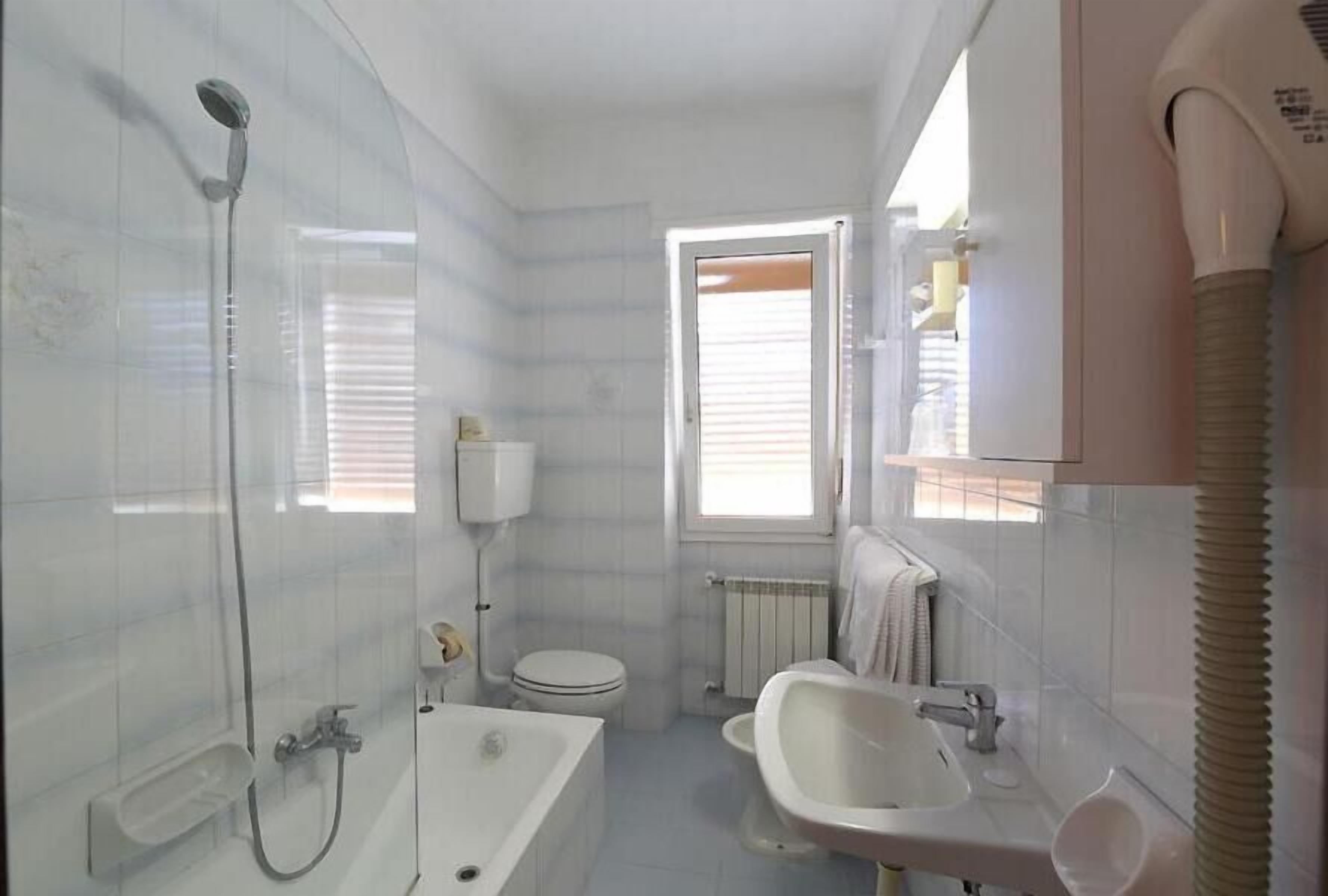 A bathroom with a shower, toilet, sink, and a window.