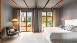 Ein Schlafzimmer mit einem großen Bett, einem Sessel, einer Lampe und Blick ins Freie durch eine Glastür.