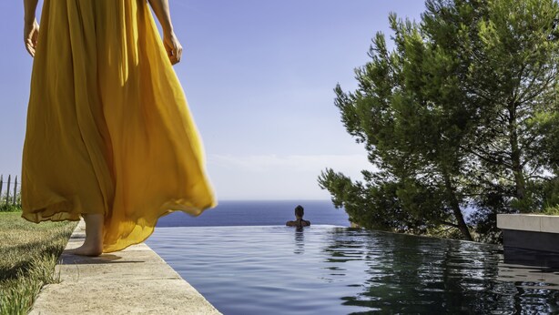 Eine Person in einem gelben Kleid steht am Rand eines Infinity-Pools mit Blick auf den Ozean.
