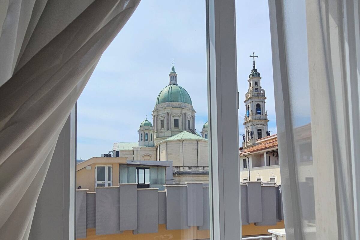 Un balcón con barandilla de metal y vistas a un edificio con cúpula verde y campanario.