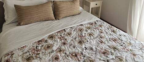 Un dormitorio con una cama grande, cabecera, mesita de noche y decoración en la pared.