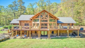 A log cabin with a large deck, multiple windows, and a stone foundation.