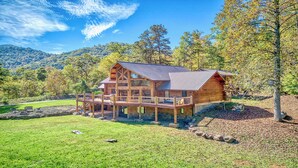 A log cabin with a deck, surrounded by a grassy yard and trees.