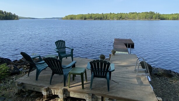 Une jetée avec des chaises et une table qui s’avance sur un lac paisible, entourée d’arbres.