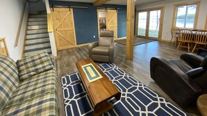 Un vaste espace de vie comprenant un escalier, un grand plafond avec une poutre en bois, un fauteuil en cuir, un canapé et une table à manger avec des chaises.