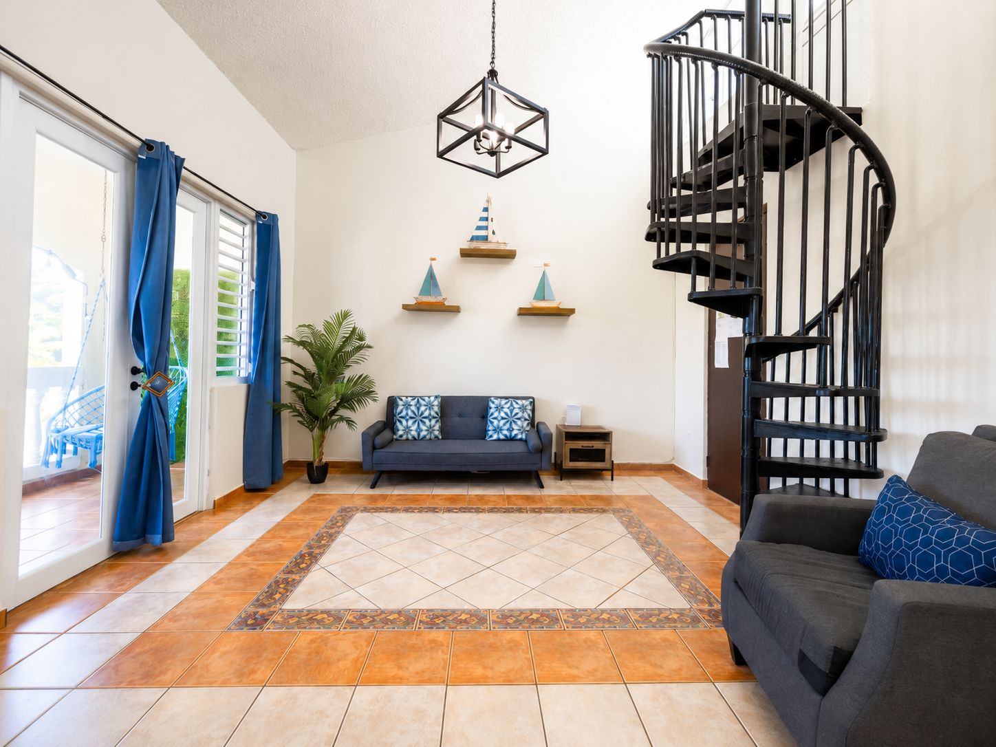 A living room with a sofa, a small table, a potted plant, a decorative wall shelf, and a spiral staircase.