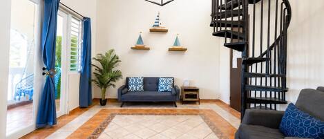 A living room with a sofa, a small table, a potted plant, a decorative wall shelf, and a spiral staircase.