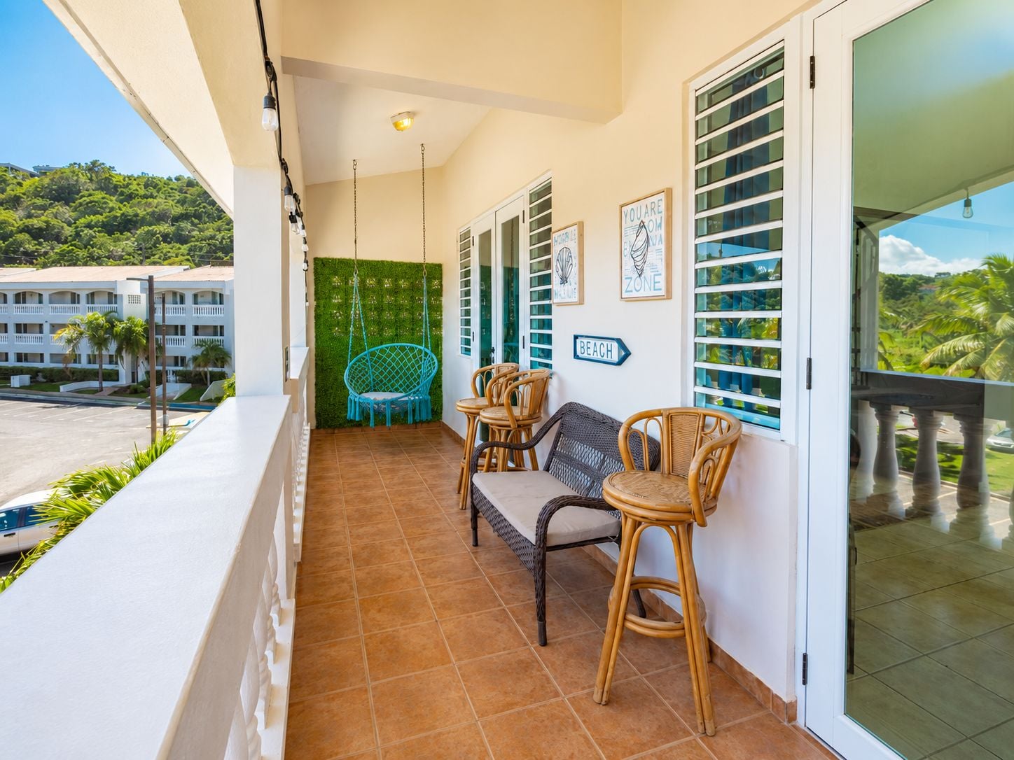 A balcony with wicker furniture, a green wall, and a sign indicating a beach direction.