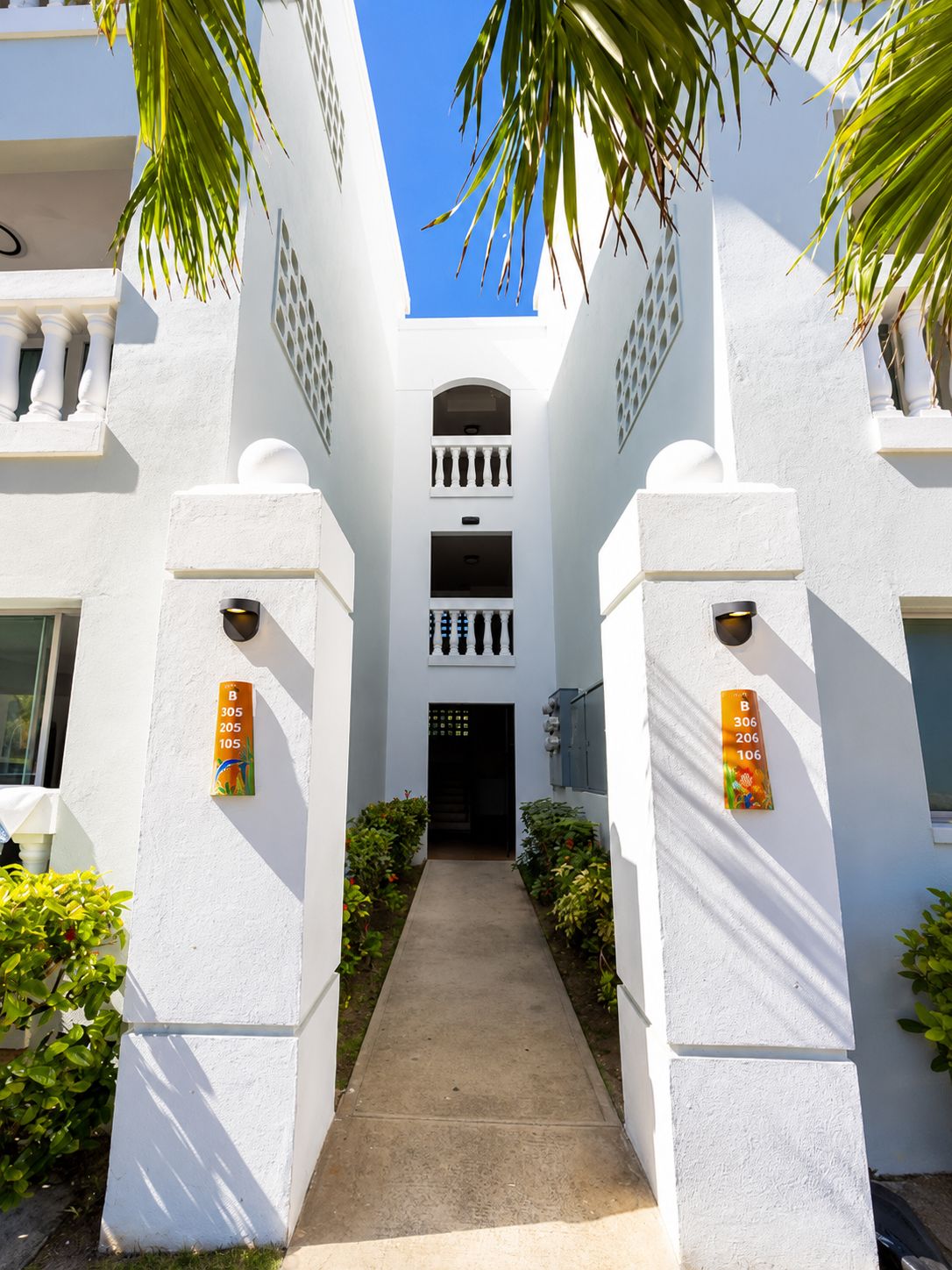 A white building with a central entrance, flanked by two pillars with apartment numbers.