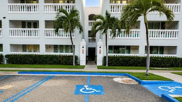 L’entrée d’un hôtel, avec une place de stationnement réservée aux personnes handicapées, des palmiers et un ciel dégagé.
