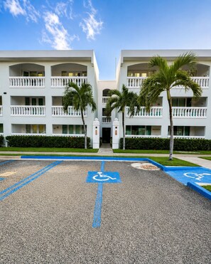 A hotel entrance with a handicap parking space, palm trees, and a clear sky. - Golden Dream Villas 306 A (Isabela)