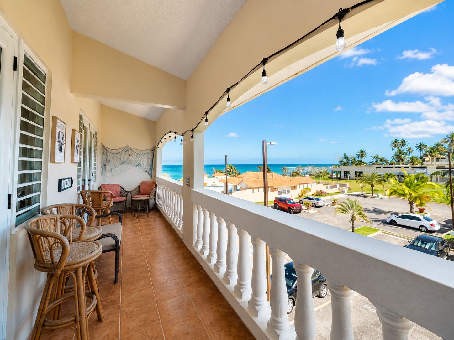 Ein Balkon mit Korbmöbeln, Blick auf den Strand und geparkte Autos.