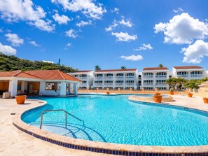 A swimming pool with a tiled deck, surrounded by buildings with a consistent architectural style. - Golden Dream Villas 306 A (Isabela)
