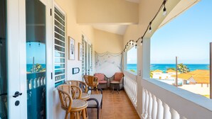 Uma varanda com móveis de vime, vista para o mar e uma porta que dá para uma área de armazenamento.