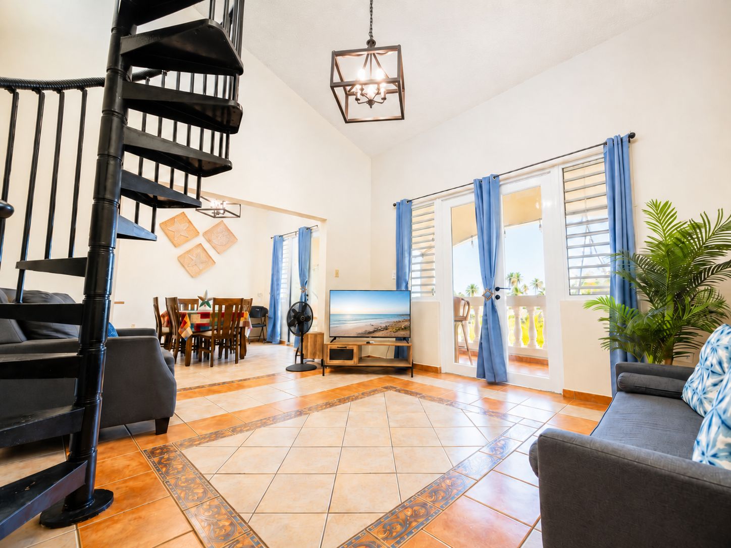 A spacious living area with a staircase, a dining table, and a large window with curtains.