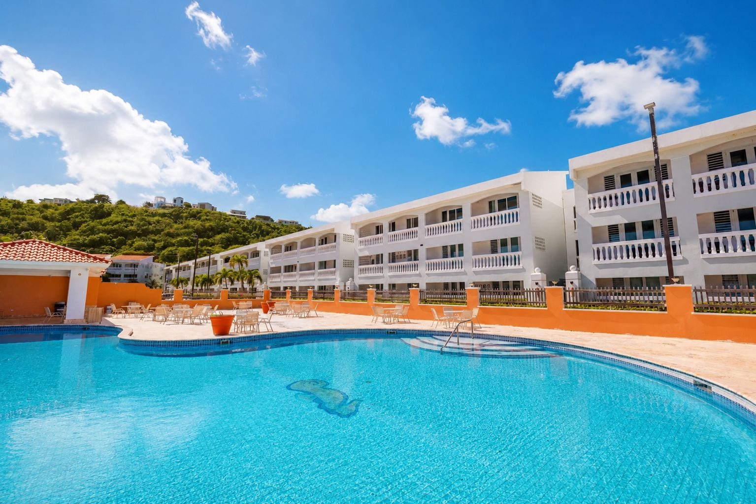 Un hotel con piscina, varios balcones y vistas a una colina verde.