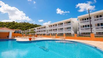 Un hotel con piscina, varios balcones y vistas a una colina verde.
