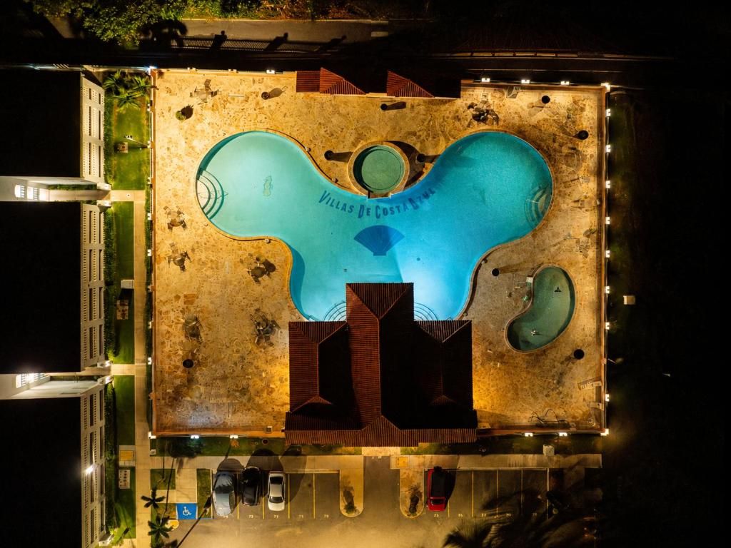 A swimming pool with a unique design, surrounded by a parking area with several cars.