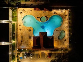 Una piscina con un diseño único, rodeada de un estacionamiento con varios coches.