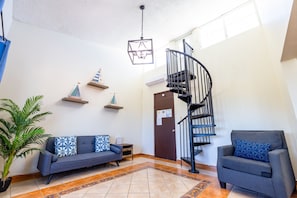 A living room with a sofa, armchair, and a spiral staircase.