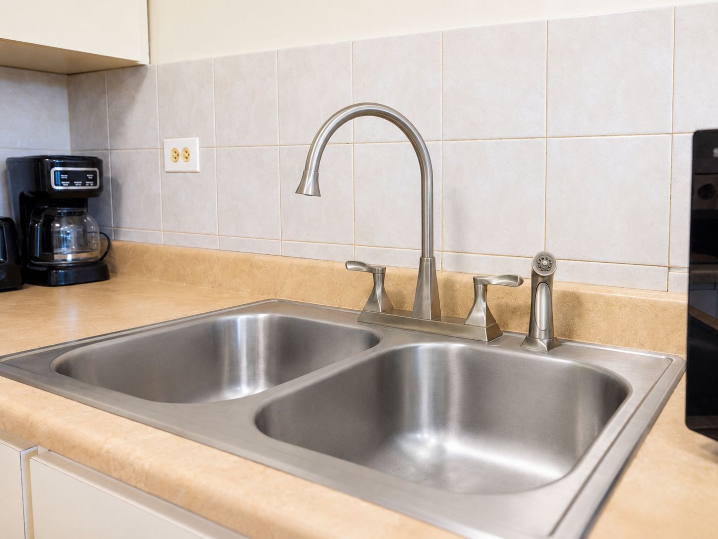 Een keuken met een dubbele rvs-spoelbak, een koffiezetapparaat en een stopcontact op de muur.