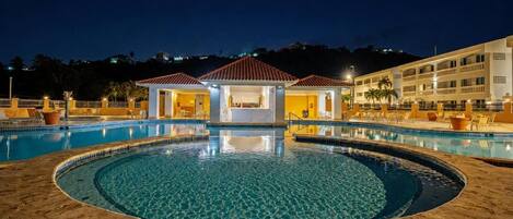A swimming pool with a circular design, a covered seating area, and a building in the background.
