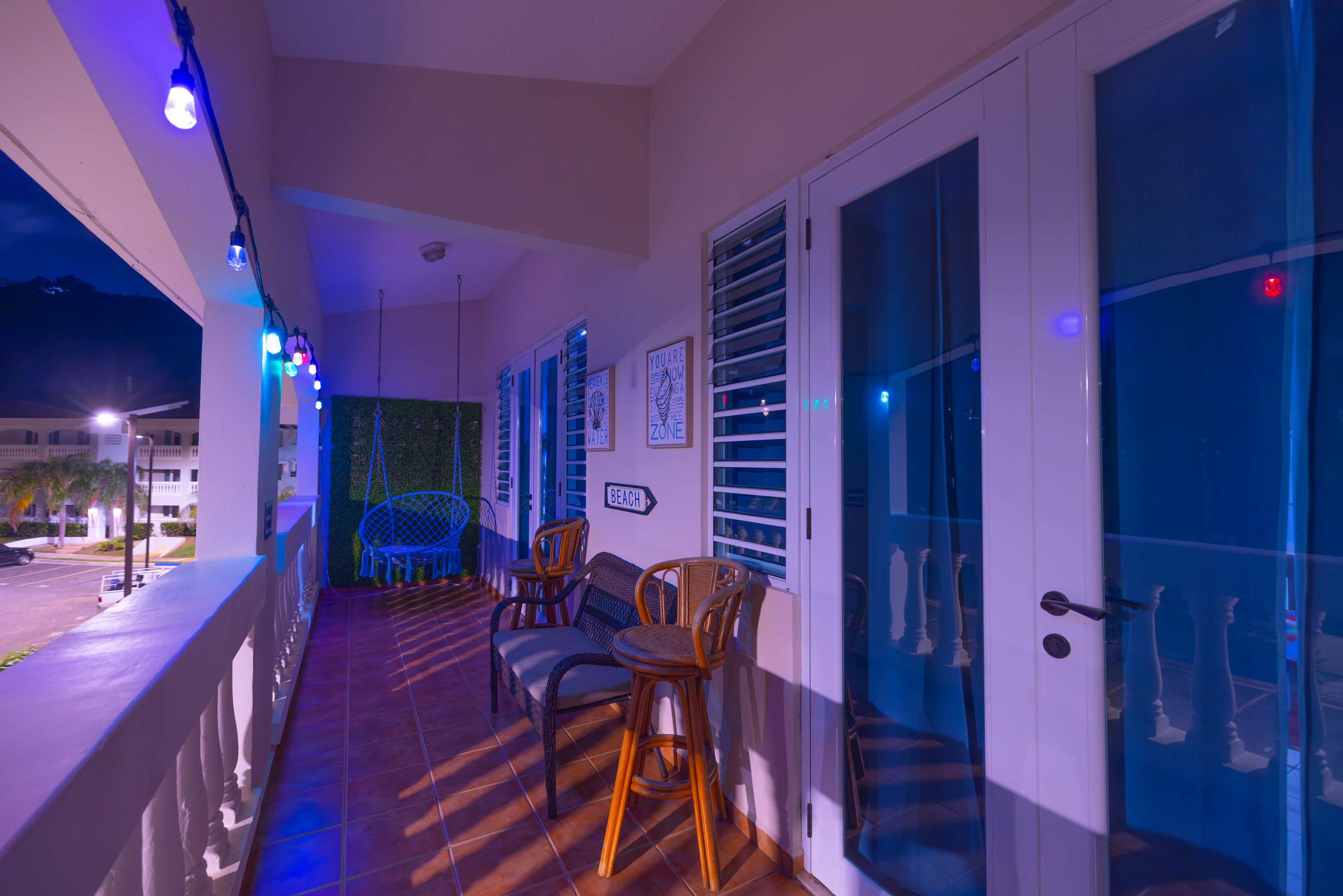 A balcony with wicker chairs, a sign indicating 'BEACH', and a view of the street at night.