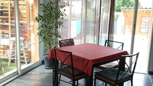 Un área de comedor con una mesa cubierta con mantel rojo, rodeada por cuatro sillas. Hay una planta en maceta a la izquierda de la mesa.