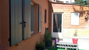 Un edificio con fachada de madera, un pequeño jardín con césped artificial y plantas en macetas.