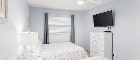 A bedroom with two beds, a ceiling fan, a TV, a dresser, and a window with curtains.