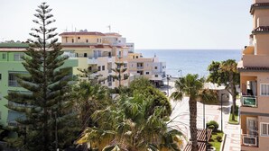 A coastal residential area with multi-story buildings, a clear view of the sea, and palm trees. - Home2Book Sea Front Attic Las Galletas (Costa del Silencio)