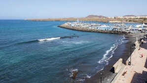 A coastal marina with boats docked, a sandy beach, and a rocky breakwater. - Home2Book Sea Front Attic Las Galletas (Costa del Silencio)