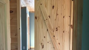 A wooden interior with a large barn-style door, a ceiling fan, and a hallway leading to another room.