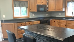 A kitchen with wooden cabinets, a black countertop, and a central island with two bar stools.