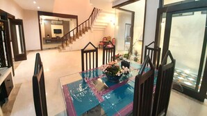 Un amplio salón con una mesa de comedor de vidrio, una escalera que conduce a otra habitación y vistas a través de un gran ventanal.
