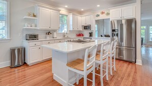 Una cocina moderna con armarios blancos, un refrigerador de acero inoxidable y una isla central con taburetes de bar.