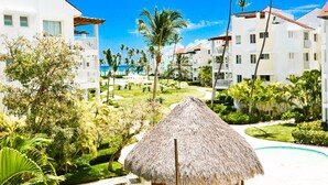 A resort with a thatched-roof hut, palm trees, and a pool. - Playa Turquesa A-302 Premier Beachfront Ocean View 50mbps Wifi (Punta Cana)