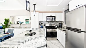 A modern kitchen with white cabinets, stainless steel appliances, a marble countertop, and a central island. - Playa Turquesa A-302 Premier Beachfront Ocean View 50mbps Wifi (Punta Cana)