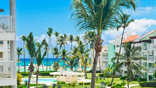 A resort with a pool, palm trees, and a view of the ocean. - Playa Turquesa A-302 Premier Beachfront Ocean View 50mbps Wifi (Punta Cana)