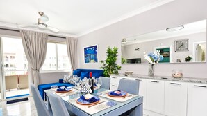 A modern dining area with a glass table, blue and white decor, and a view of the city. - Playa Turquesa A-302 Premier Beachfront Ocean View 50mbps Wifi (Punta Cana)