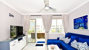 A modern living room with a blue sofa, a flat-screen TV, and a ceiling fan. - Playa Turquesa A-302 Premier Beachfront Ocean View 50mbps Wifi (Punta Cana)