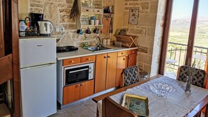 A rustic kitchen with a stone wall, wooden cabinets, a refrigerator, a stove, and a dining table with chairs. - Aelia Villa & Apartments with enchanting views of the Messara plain (Kamilari)