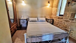 A bedroom with a metal bed frame, a nightstand, a dresser, and a stone wall. - Aelia Villa & Apartments with enchanting views of the Messara plain (Kamilari)