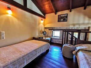 A cozy room with two beds, a small table, a fan, and a window.