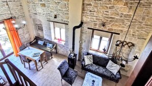 A spacious room with a stone wall, a dining area with a table and chairs, and a sofa with a hanging light fixture. - Aelia Villa & Apartments with enchanting views of the Messara plain (Kamilari)