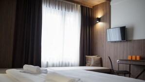 A hotel room with two beds, a TV mounted on the wall, a small table with orange objects, and a window with curtains.