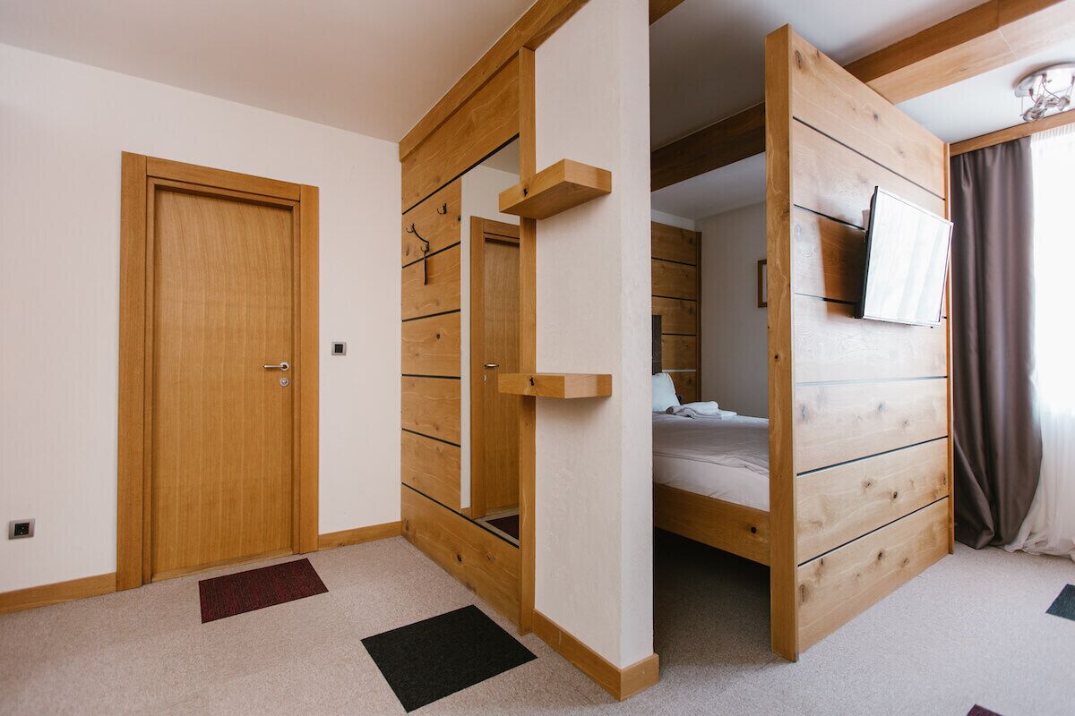 A room with a wooden wardrobe, a bed, and a TV mounted on the wall.