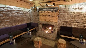 A rustic interior with stone walls, a wooden fireplace, and seating areas.